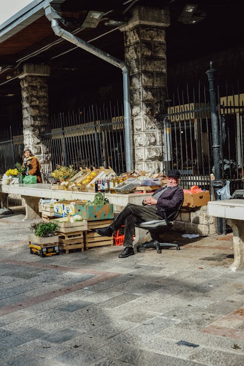 Elderly Merchant Sitting Next to Stall with Fruits on Sidewalk