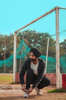 Athletic Indian man in sportswear ties his shoe at a soccer field, ready for a game.