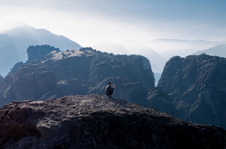 Majestic view of a man photographing the dramatic Meteora cliffs in Greece during daytime.