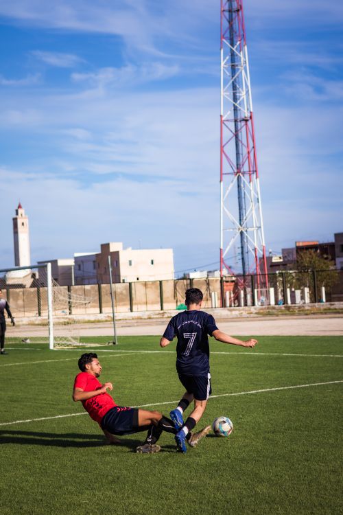 Free Two footballers in action on a sunny day, showcasing a dynamic slide tackle on the field. Stock Photo