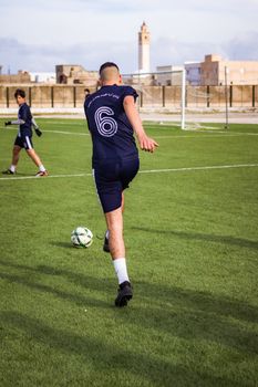 A soccer player in sportswear kicks a ball on a grass field during daytime practice.