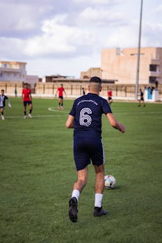 A soccer player in blue kit dribbling on a grass field during a sunny day match.