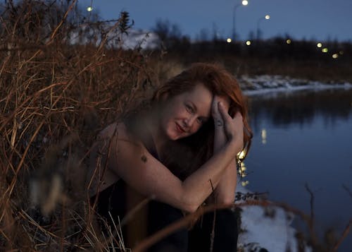 Portrait of a Long-Haired Redhead Sitting on a Lakeshore at Night
