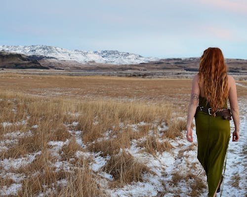 Back View of a Woman in a Dress Walking on a Snowy Field in Mountains 