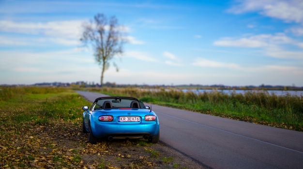 Blue Mazda Miata convertible on a scenic countryside road in Szczerbaków, Poland.