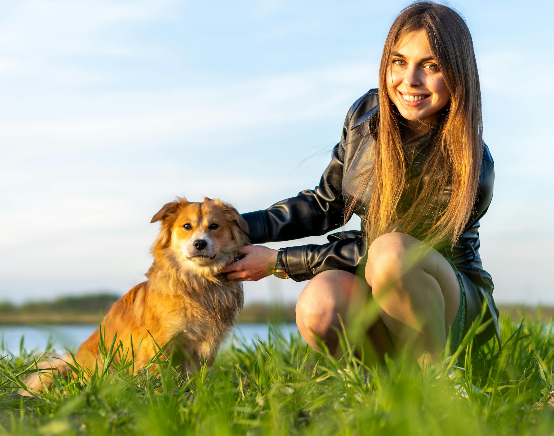 Portrait of a Pretty Brunette Crouching on the Grass with a Dog