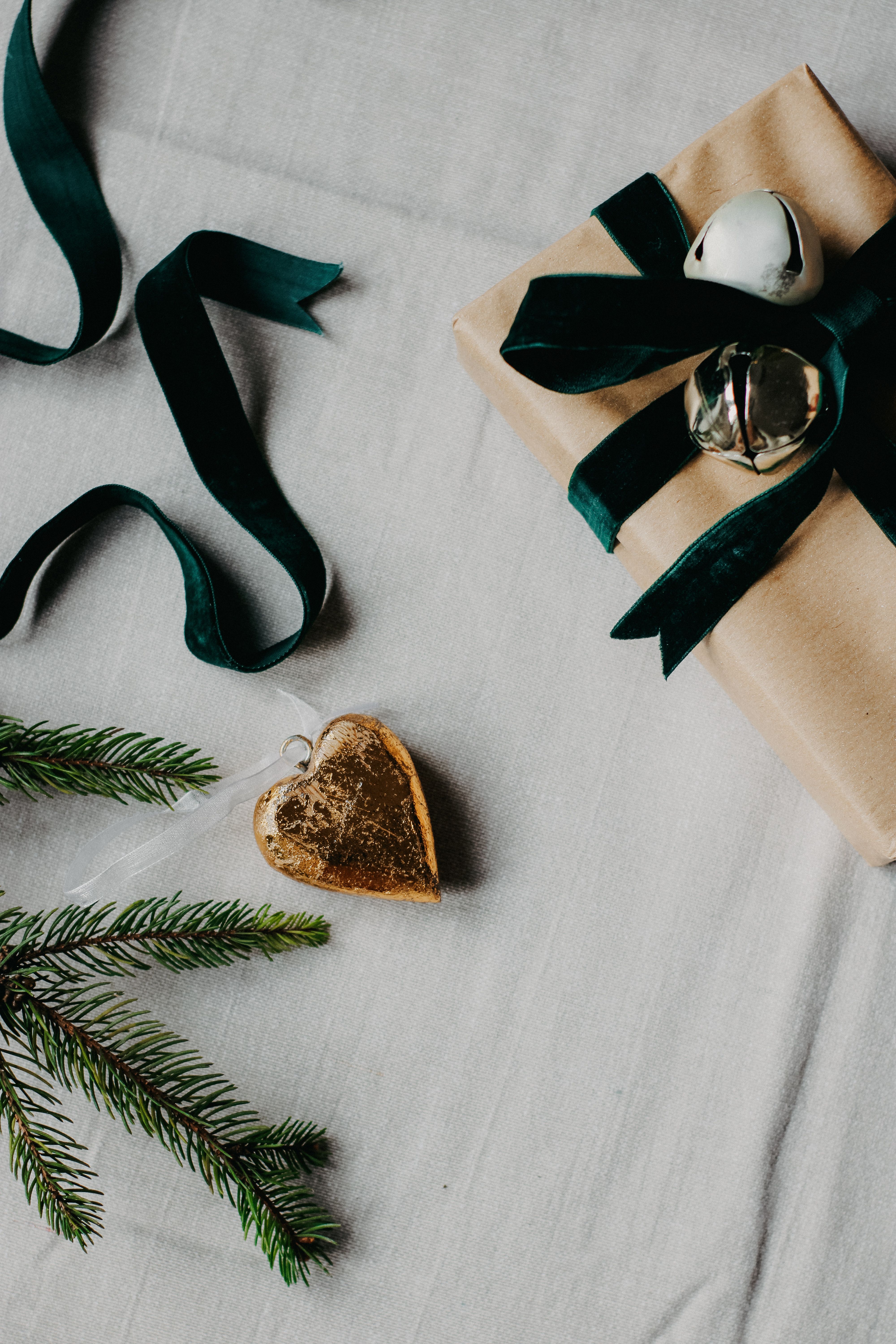 A beautifully wrapped Christmas gift with green ribbons, ornaments, and a pine twig.