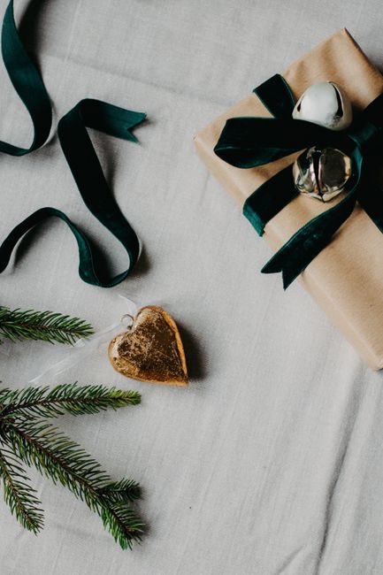 A beautifully wrapped Christmas gift with green ribbons, ornaments, and a pine twig.