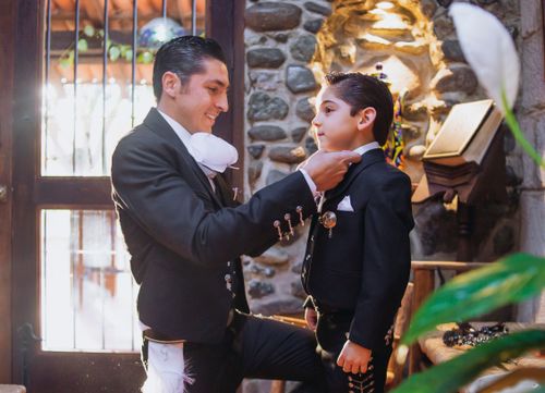 Free A father helps his son adjust a tie in a traditional Mexican suit indoors in León, Mexico. Stock Photo