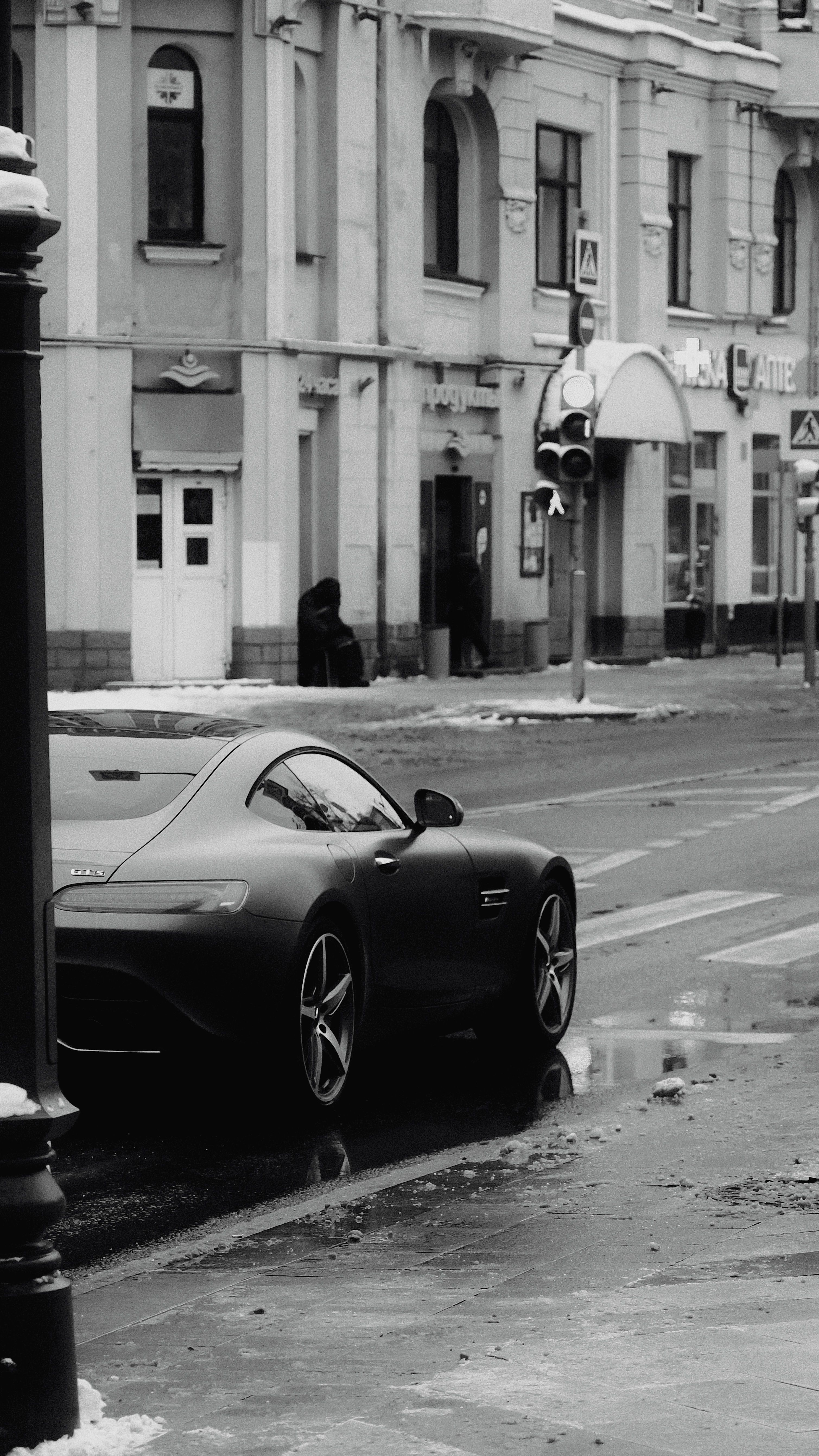 Black luxury car parked on a snowy city street in winter, reflecting classic architecture.