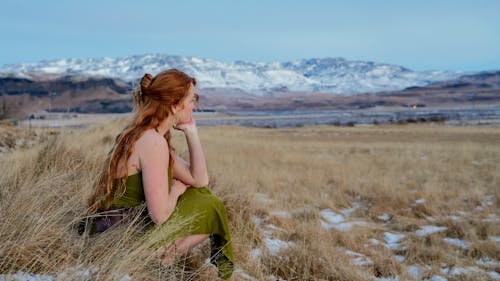 Woman in Green Dress Sitting on Grassland in Winter