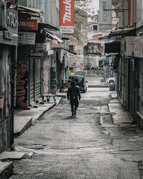 Hooded Man with a Backpack Walking Down an Alley of Closed Shops