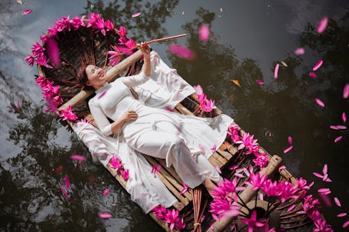 Young Woman in White Dress Lying on Boat with Pink Flowers