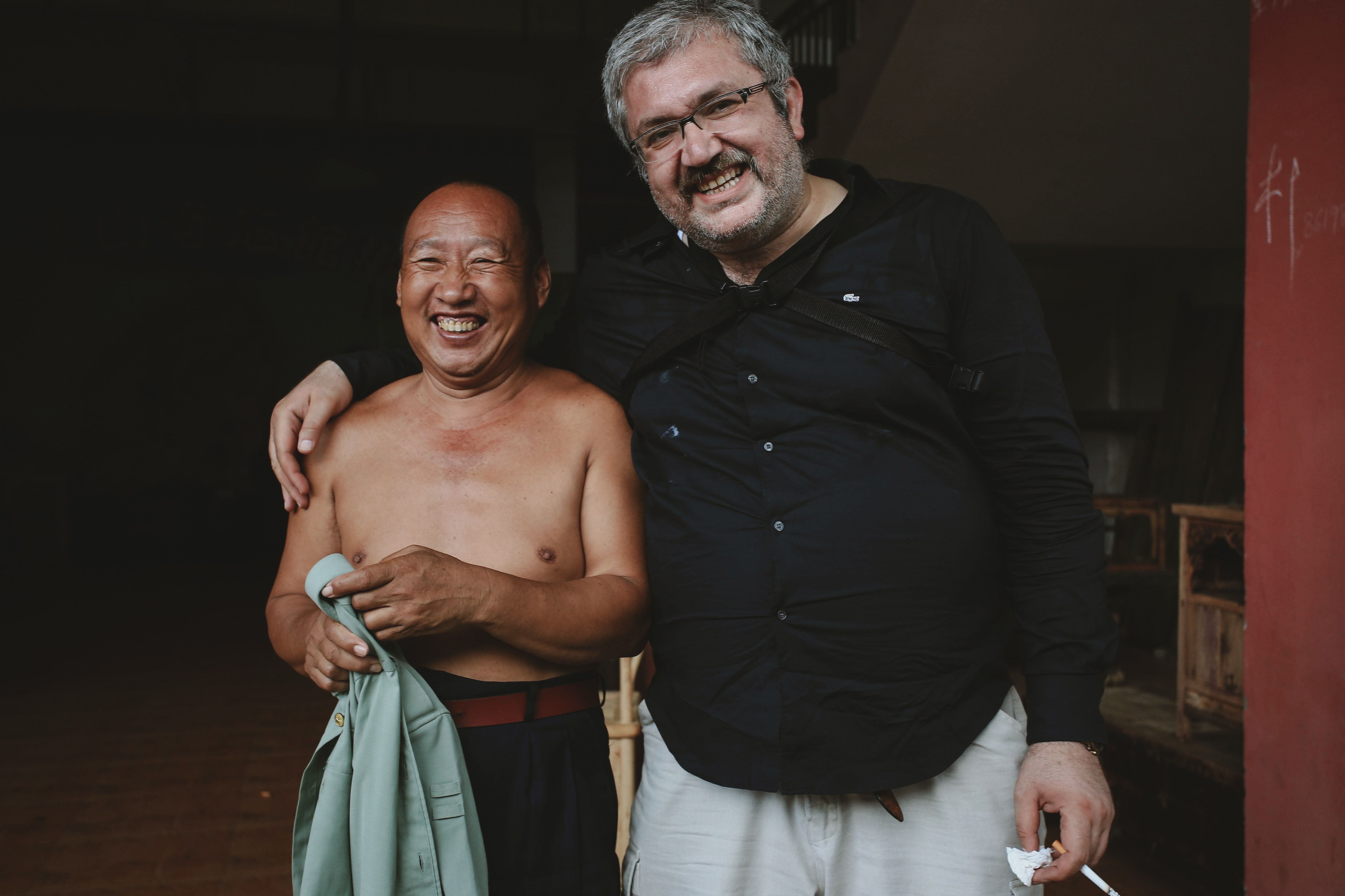 Two smiling men standing and embracing indoors, capturing a moment of friendship.