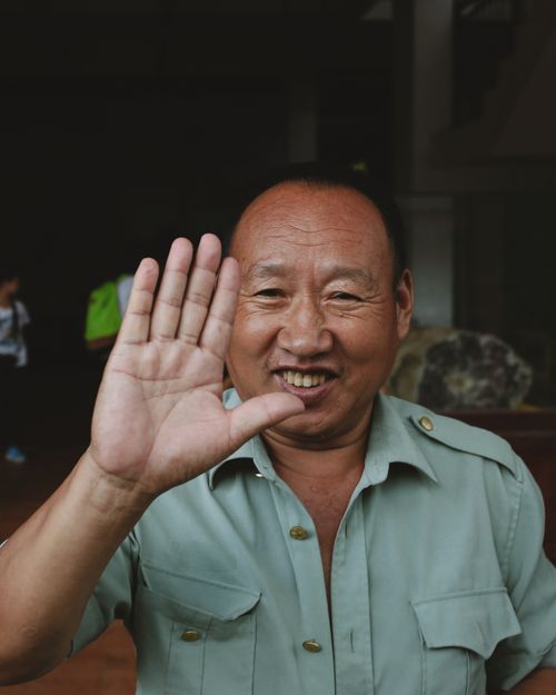 Free Portrait of a senior man smiling and waving his hand in a friendly gesture outdoors. Stock Photo