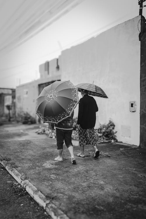 Black and White Photo of Two Women with Umbrellas Walking on a Street