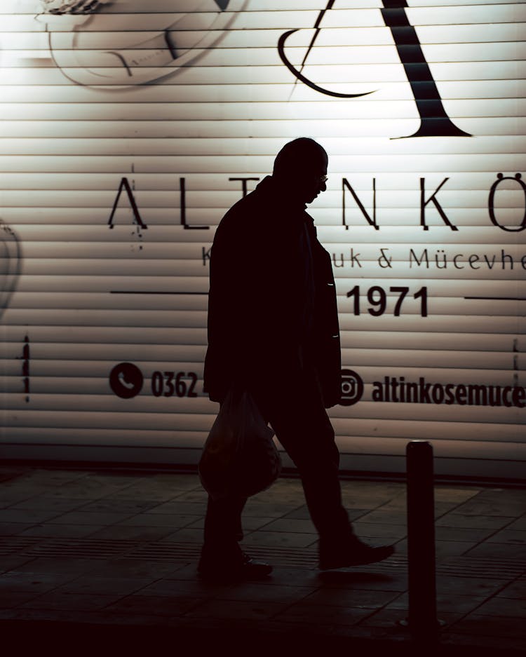 Silhouette Of A Man Walking Past A Store Wall On A Night Street