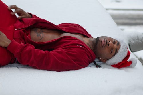 Man in a Red Tracksuit and a Santa Hat Lying on a Blanket Spread in the Snow