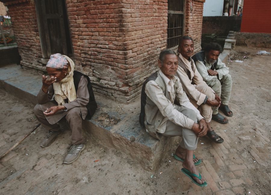 Elderly Nepali men sitting by a red brick wall in an urban setting, Kathmandu, Nepal.