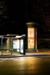 Illuminated poster column and bus shelter at night