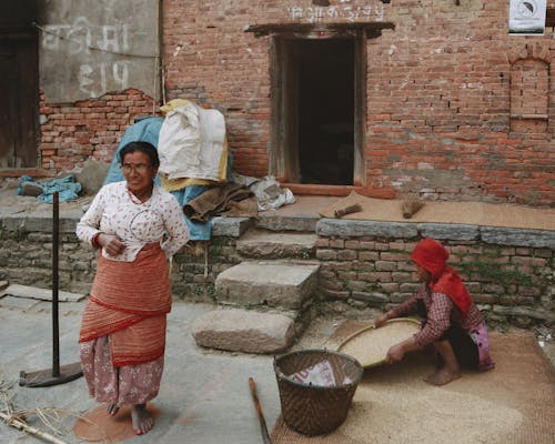 Elderly Woman Drying Rice Outside of a Building