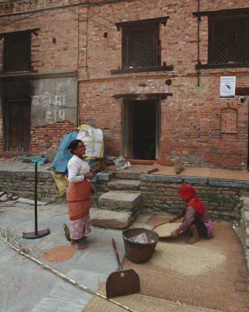 Free Two women working with grains outside a rustic brick building. Stock Photo
