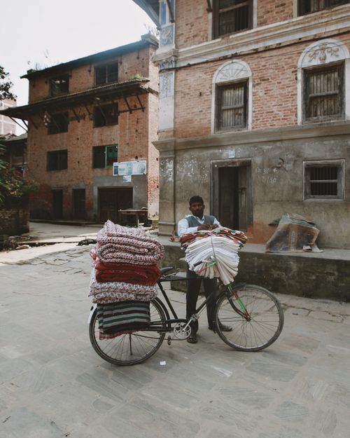 Free A man stands with a bicycle laden with colorful blankets on an urban street. Stock Photo