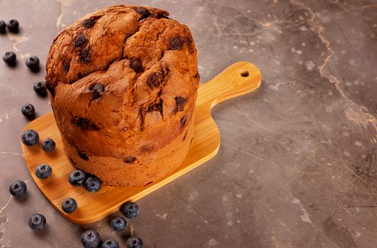 Delicious homemade blueberry cake on a wooden board surrounded by fresh blueberries.