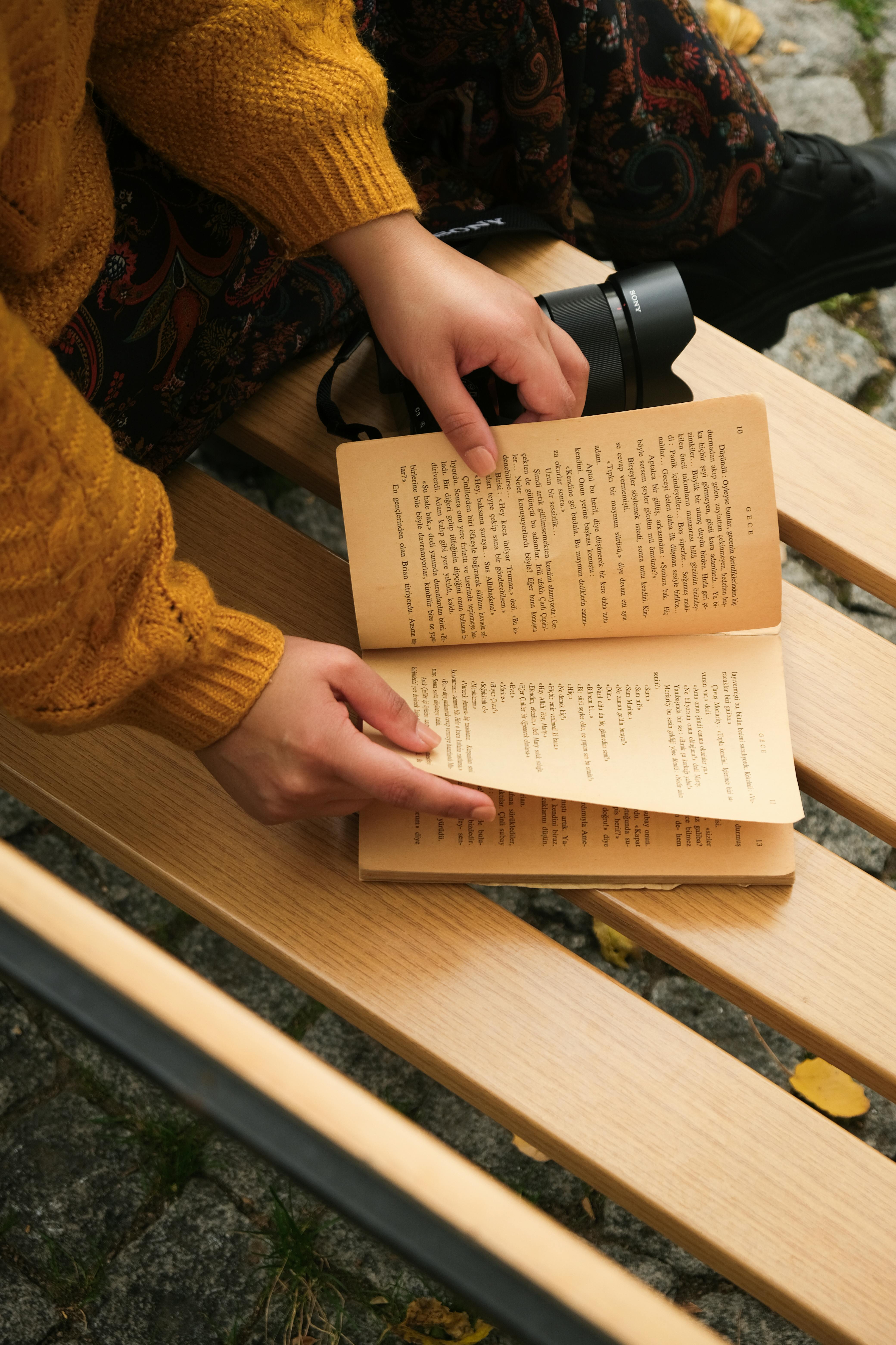 A person reading a book on a wooden bench, capturing the cozy feel of autumn.