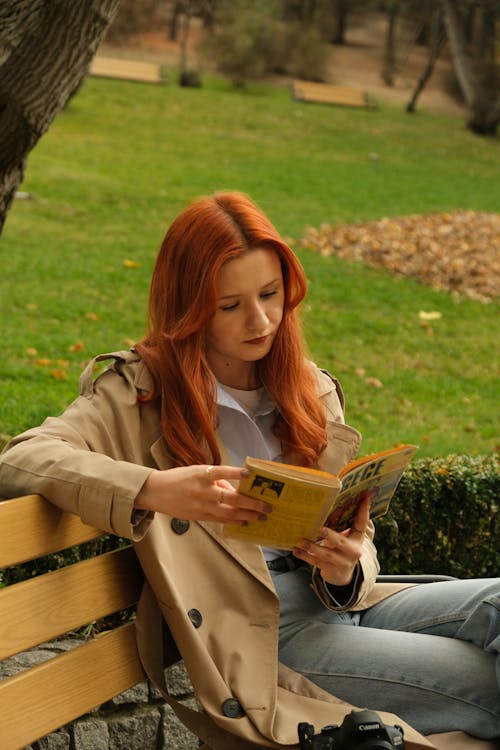 Redhead in a Coat Reading a Book on a Park Bench
