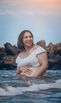 Smiling pregnant woman in ocean with rocks, enjoying a relaxing day at Coveñas, Colombia.