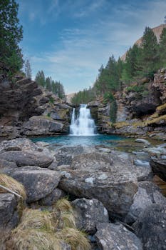 Beautiful waterfall cascade in Gradas de Soaso, surrounded by rocks and trees, under a clear blue sky.