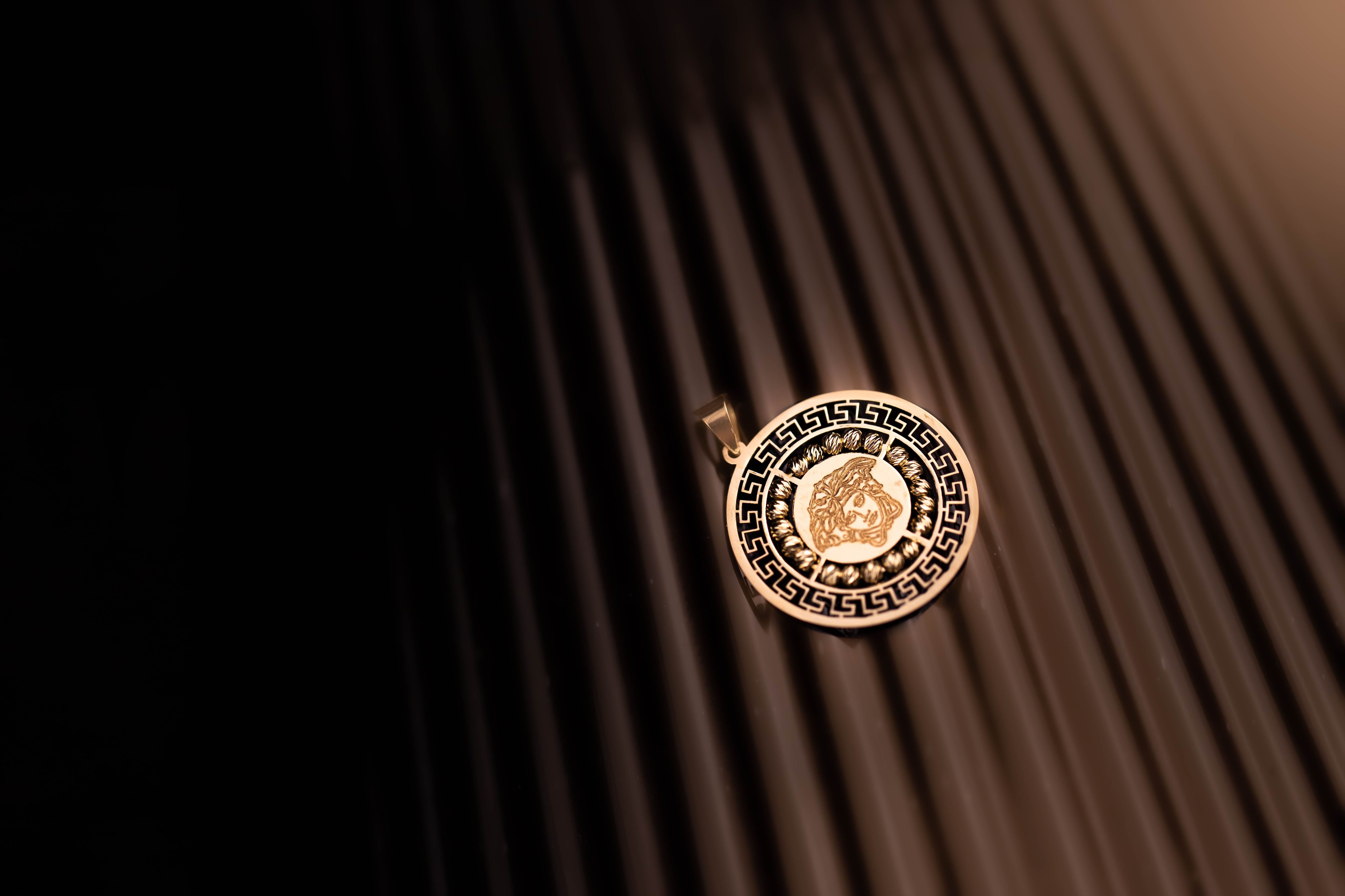 A beautifully ornamented golden pendant with intricate patterns, lying on a black surface.
