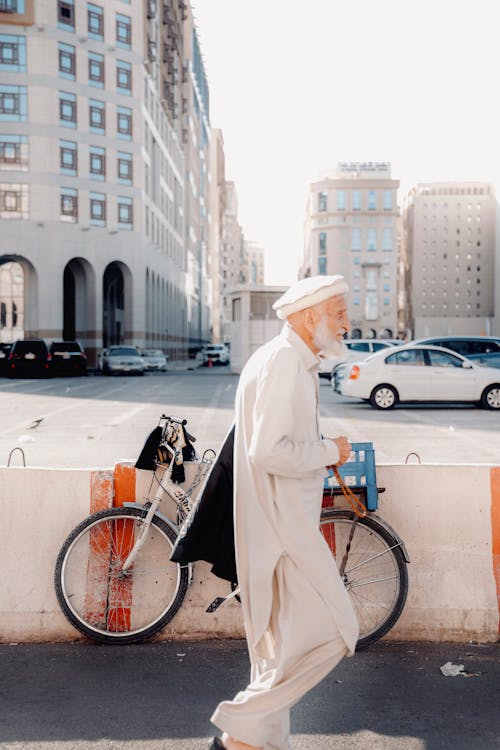 Elderly Man in White Gown Walking on Sidewalk
