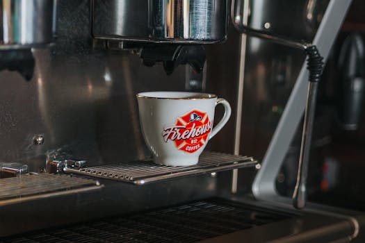 A coffee cup with Firehouse branding under an espresso machine, ready to brew.