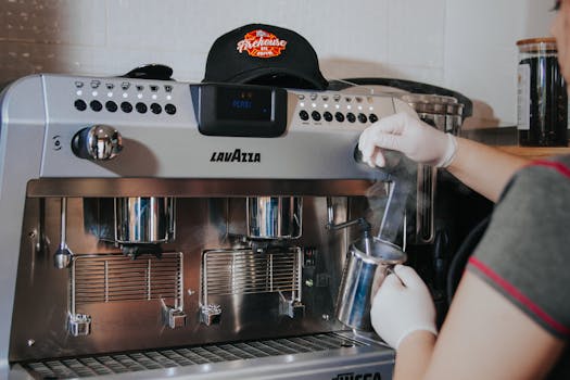 Barista steaming milk with Lavazza espresso machine, indoors, wearing gloves.