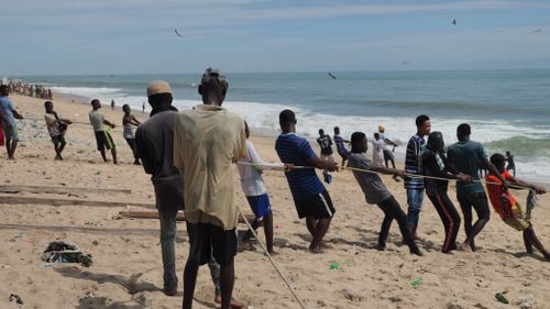 Free Men on the beach engaged in a tug of war, displaying teamwork and strength. Stock Photo