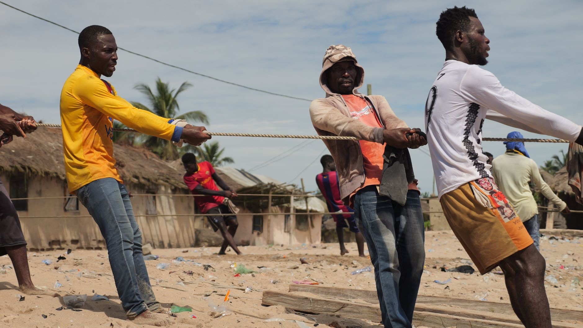 Men engaged in a spirited tug of war on a sunny beach, showcasing teamwork and strength.