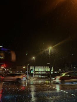 Cars pass by a rainy intersection at night in Würzburg, showcasing urban nightlife and reflections.