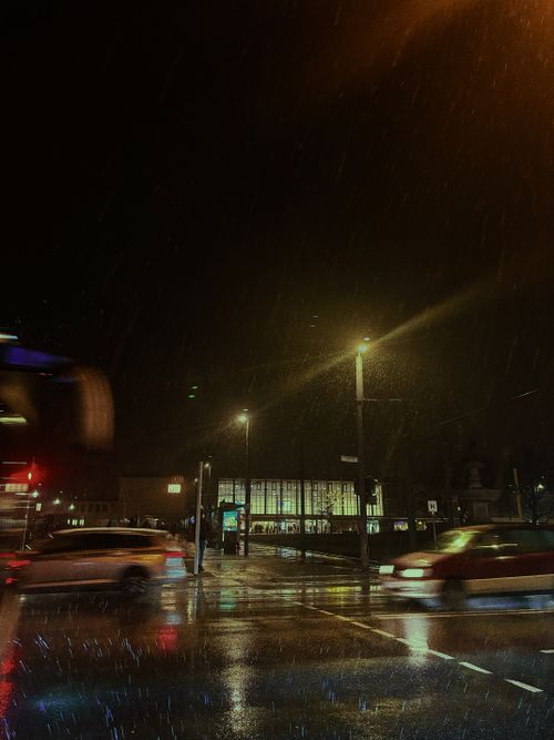 Free Cars pass by a rainy intersection at night in Würzburg, showcasing urban nightlife and reflections. Stock Photo