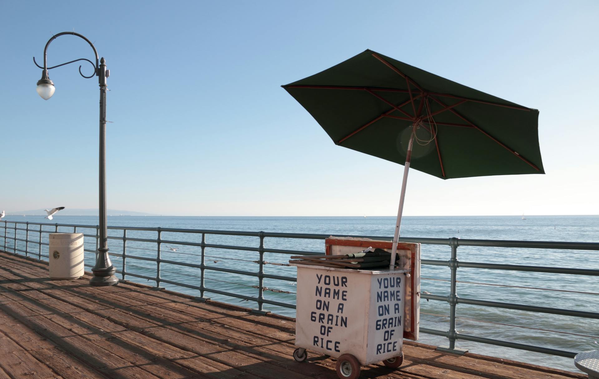 Vendor cart and umbrella on Santa Monica Pier with ocean view. Perfect relaxation spot.