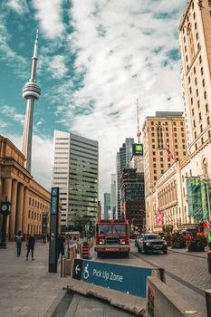 Urban streetscape featuring the CN Tower in downtown Toronto with city life and vehicles.