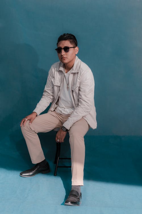 Man in Sunglasses and a Casual Outfit Sitting on a Chair on Blue Background 