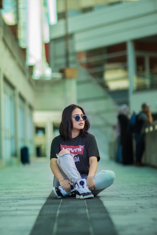 A girl sitting on the ground wearing a t - shirt and sunglasses