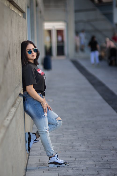 A woman leaning against a wall wearing jeans and a t - shirt
