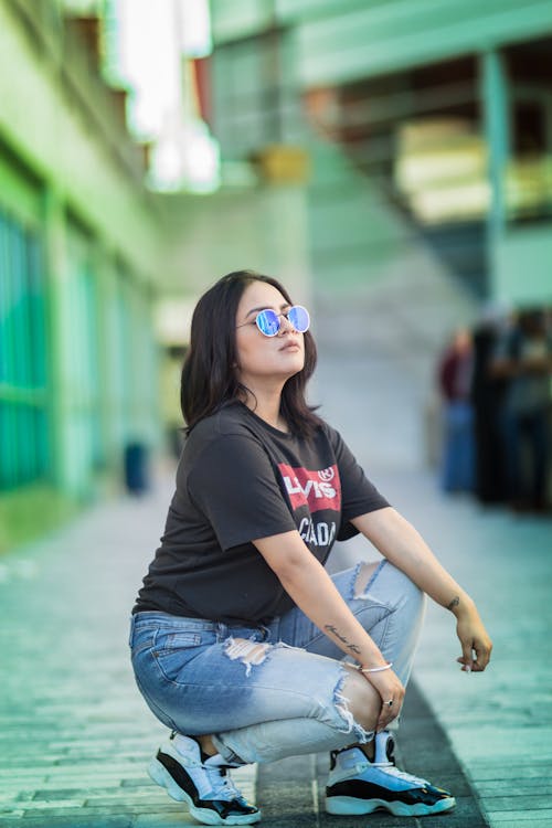 A woman in a black shirt and jeans squatting on the ground