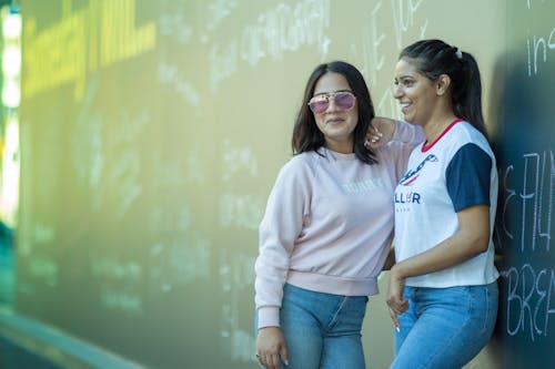 Two young women standing next to each other in front of a wall