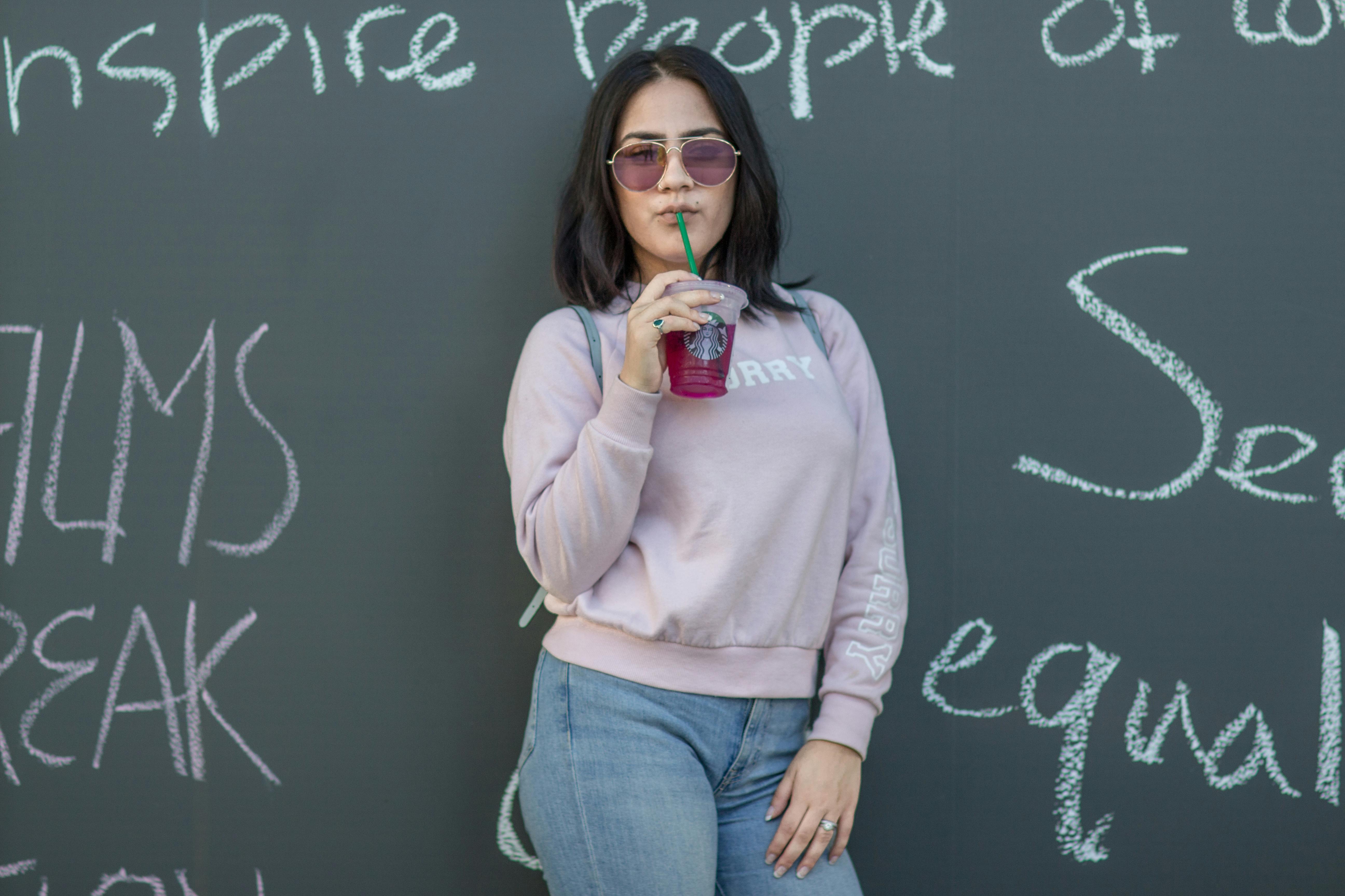 a woman in a sweatshirt and sunglasses is standing next to a chalkboard