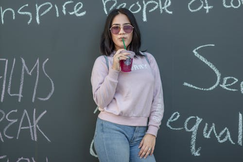 A woman in a sweatshirt and sunglasses is standing next to a chalkboard