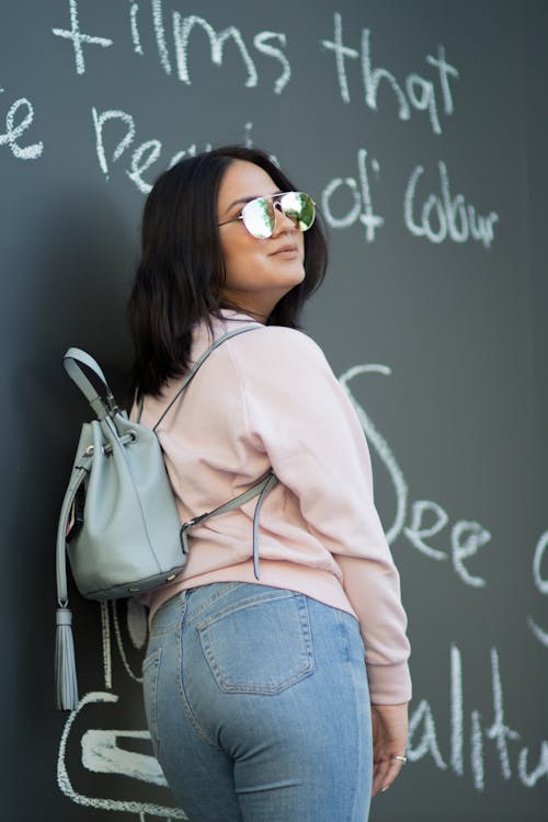 A woman in jeans and a pink sweater leaning against a wall